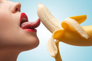 A face of porn star licking a half-peeled yellow banana